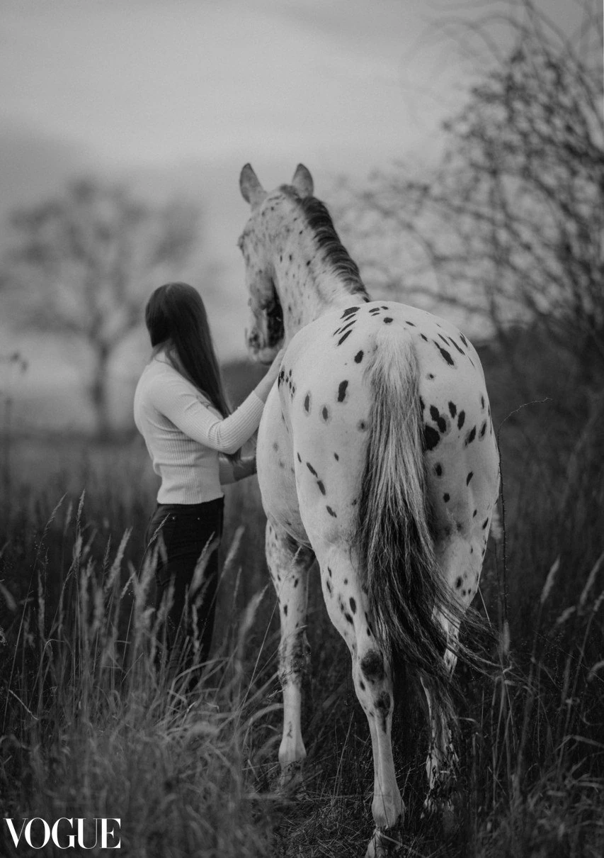 Žena kráča lúkou vedľa škvrnitého koňa, čiernobiela fotografia