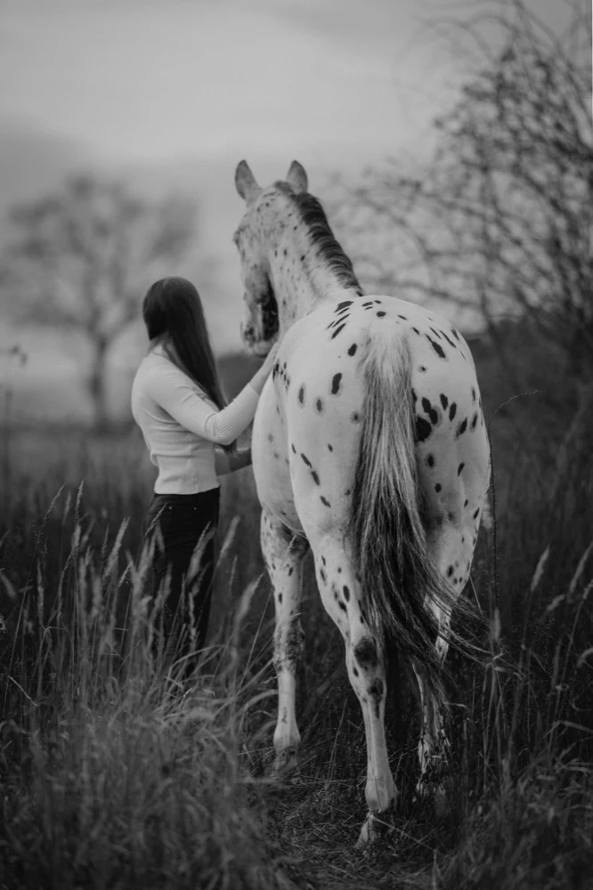 Čiernobiela fotografia ženy a škvrnitého koňa v poli