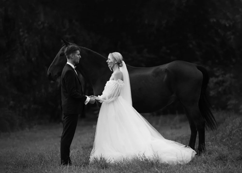 Novomanželia sa držia za ruky vedľa koňa, čiernobiela fotografia